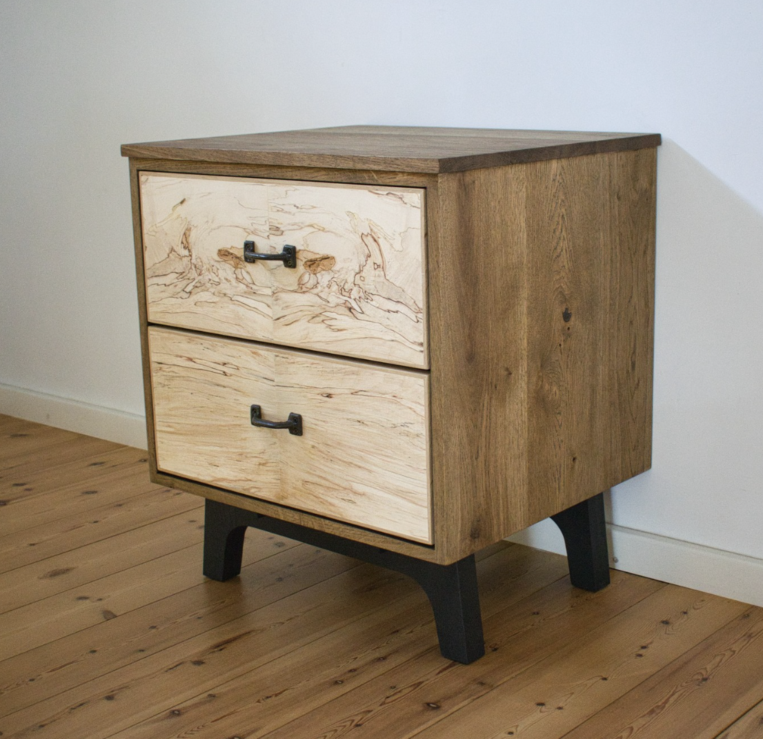 Compact eiken nachtkastje met kastanjekleurige fronten naast een bed